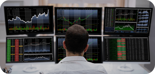 Trader monitoring multiple financial market screens in a trading room.