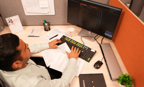 A professional working at an office desk typing on a keyboard in front of a computer monitor displaying financial data